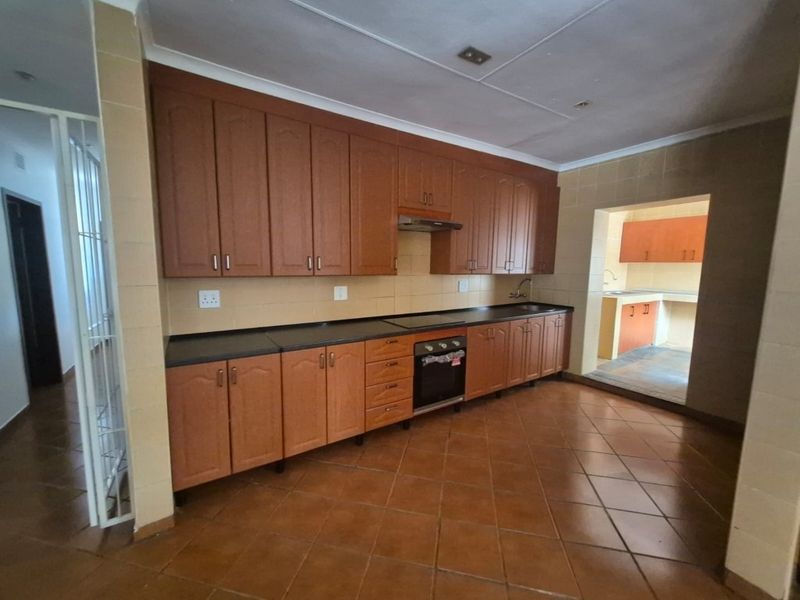 A functional kitchen featuring wooden cabinetry, built-in oven, extractor fan, and tiled flooring, with an adjacent scullery area.