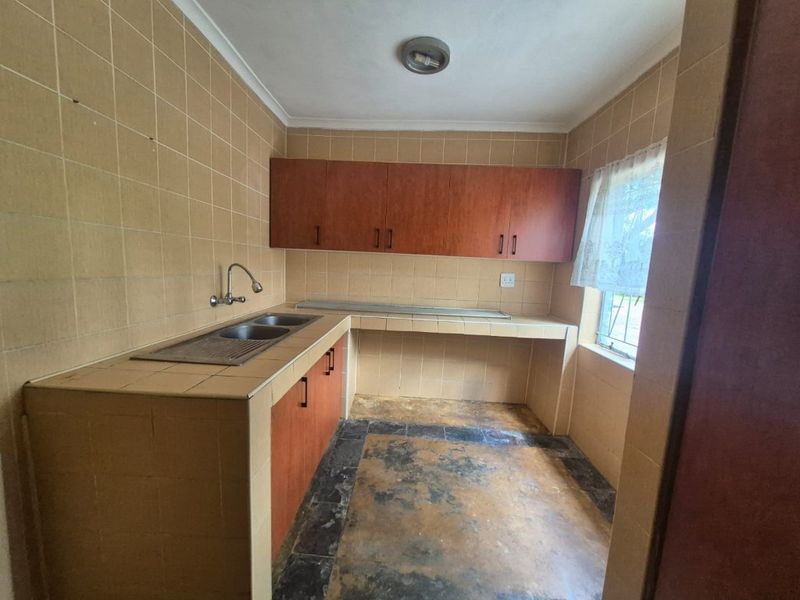 A dated kitchen featuring tiled countertops, a double bowl sink, and wooden cabinetry, requiring modernization to improve functionality and aesthetic appeal.