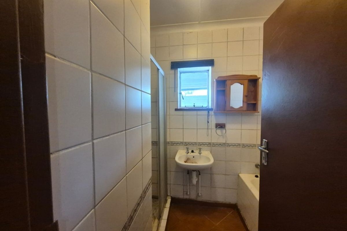 A dated bathroom featuring a wall-mounted basin, shower enclosure, and bathtub with tiled finishes throughout.