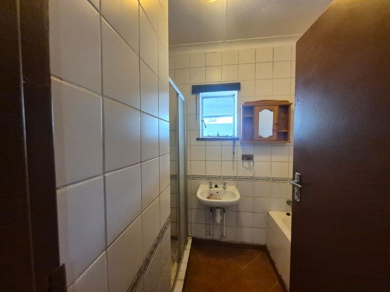A dated bathroom featuring a wall-mounted basin, shower enclosure, and bathtub with tiled finishes throughout.