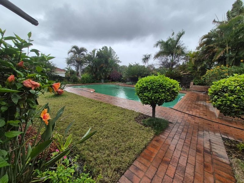 A private outdoor pool area featuring a swimming pool surrounded by brick paving and established garden landscaping.