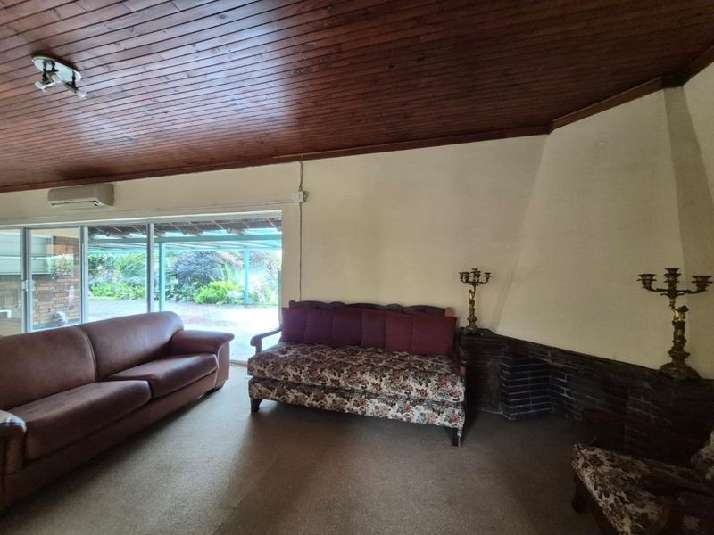 Spacious living room featuring a timber-clad ceiling, brick fireplace, and large sliding glass doors providing access to the outdoor area.