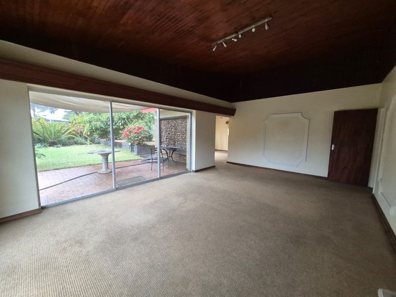 Spacious living area featuring a timber-clad vaulted ceiling, carpeted flooring, and large sliding glass doors providing direct access to the rear garden.