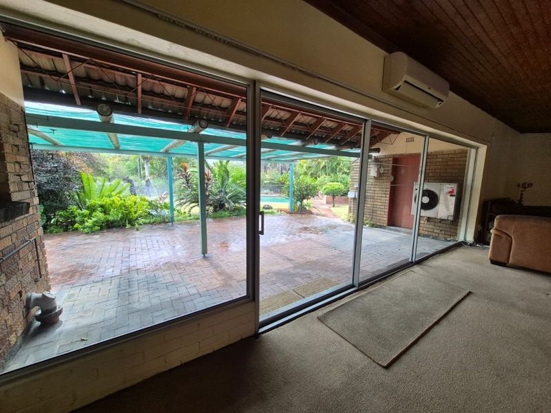 Spacious living area featuring large sliding glass doors that open onto a covered patio, timber-clad ceilings, and a wall-mounted air conditioning unit.