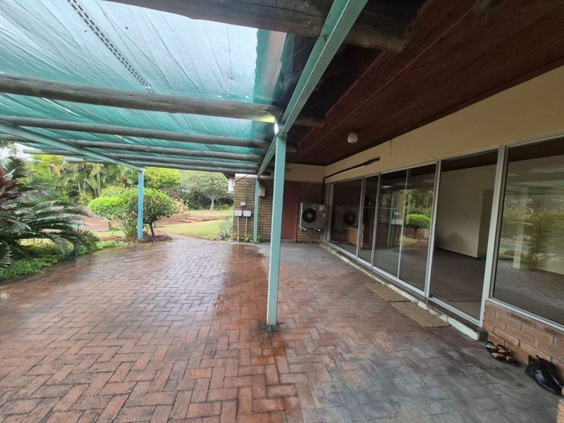 A covered brick-paved patio area featuring a timber ceiling and large sliding glass doors providing access to the interior living space.