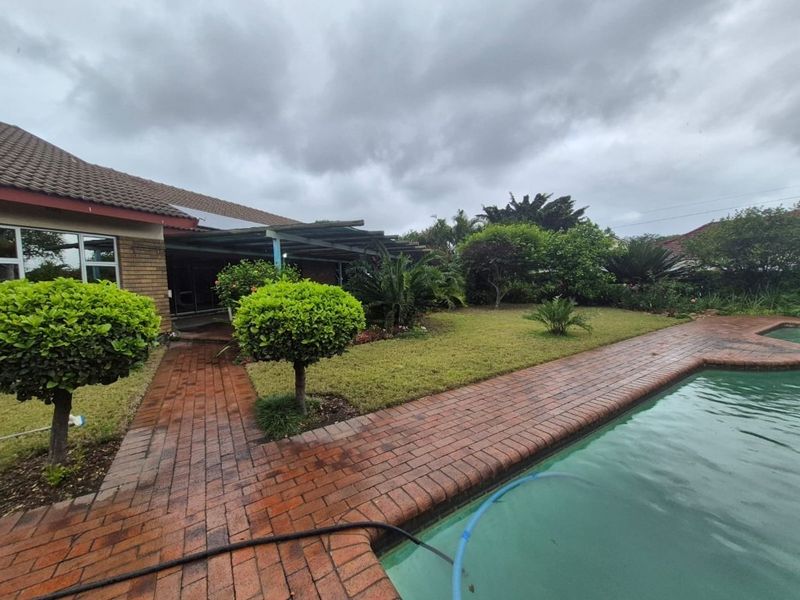 Rear garden area featuring a swimming pool, brick paved surround, and a covered patio attached to the main house structure.