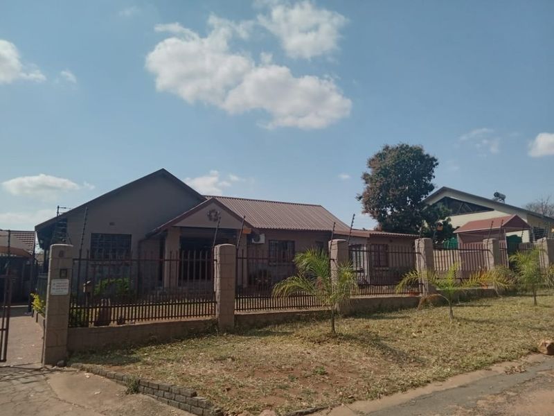Front view of a single-story house featuring a metal roof, covered entrance porch, and a secure perimeter wall with electric fencing.