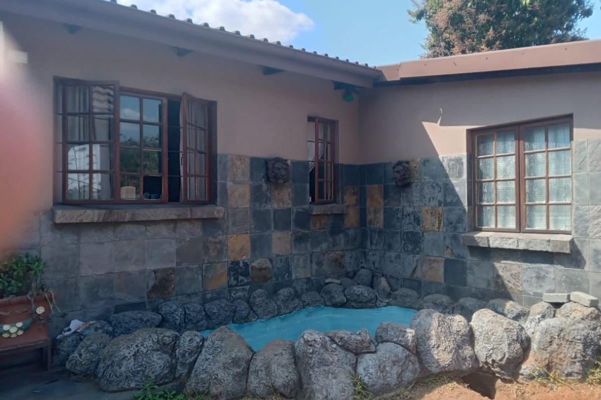 Rear exterior view featuring stone-clad walls, timber-framed windows, and a decorative rock-bordered water feature in the garden area.
