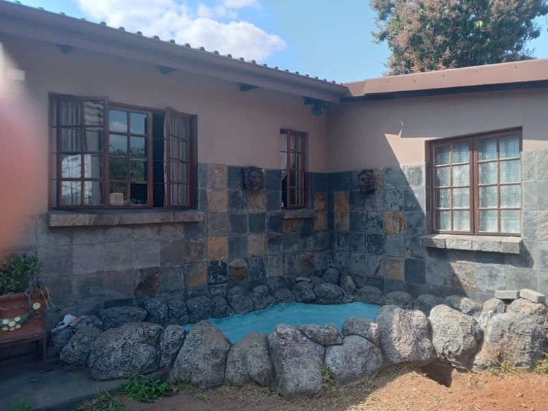 Rear exterior view featuring stone-clad walls, timber-framed windows, and a decorative rock-bordered water feature in the garden area.