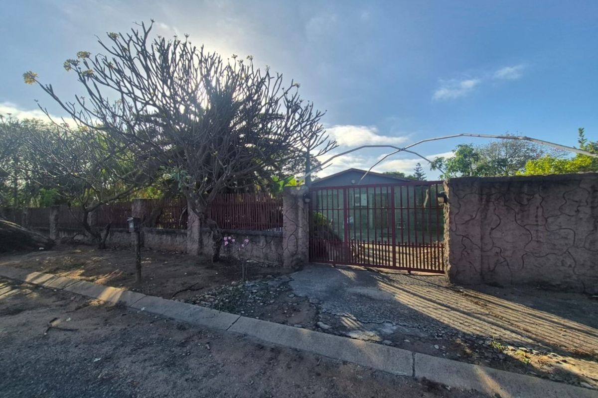 Front view of the property featuring a metal security gate, perimeter wall, and driveway access from the street.