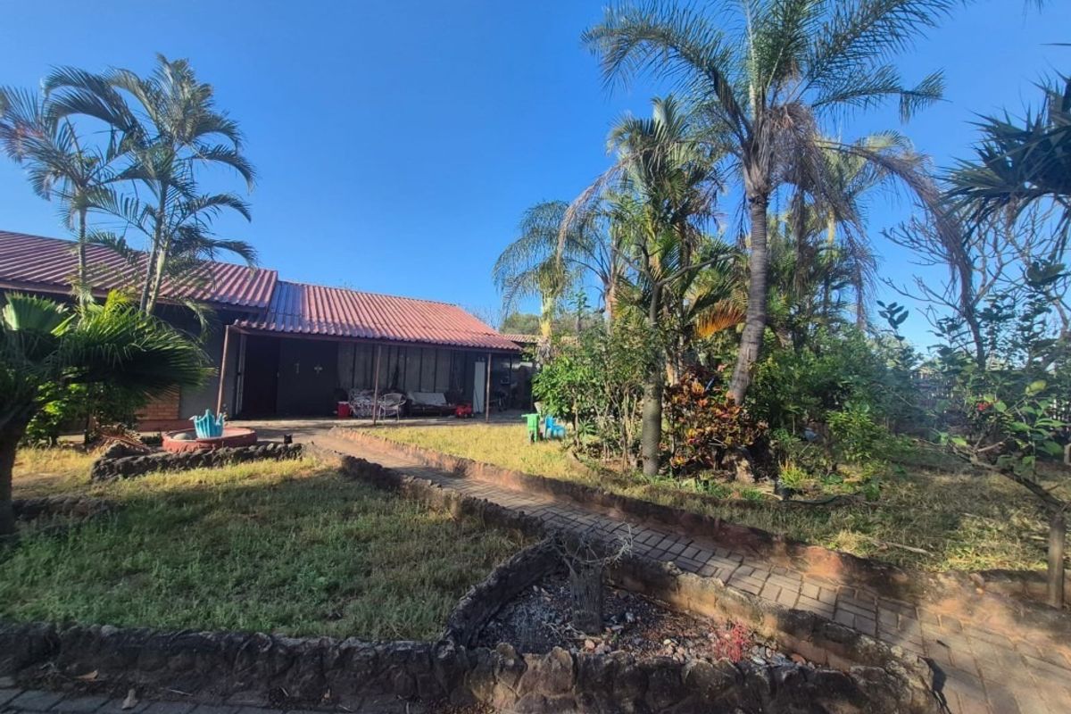 Rear view of the property featuring a covered patio, tiled roof, and a landscaped garden with paved pathways.