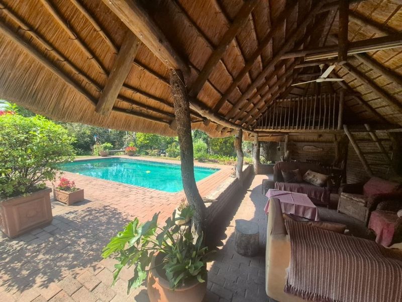 Outdoor entertainment area featuring a swimming pool, brick patio, and a large thatched roof structure with a mezzanine level.