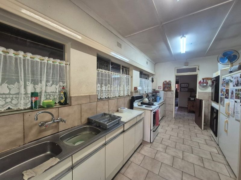 A functional, dated kitchen featuring tiled flooring, a double bowl stainless steel sink, and built-in cabinetry with a freestanding stove.