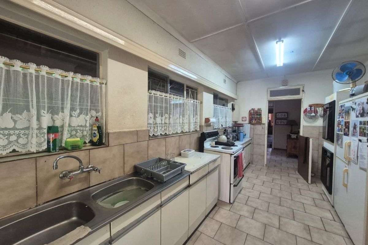 A functional, dated kitchen featuring tiled flooring, a double bowl stainless steel sink, and built-in cabinetry with a freestanding stove.