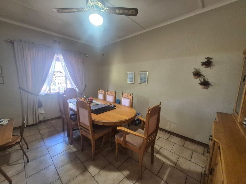 A functional dining room featuring tiled flooring, a ceiling fan, and natural light from a window with curtain rails.
