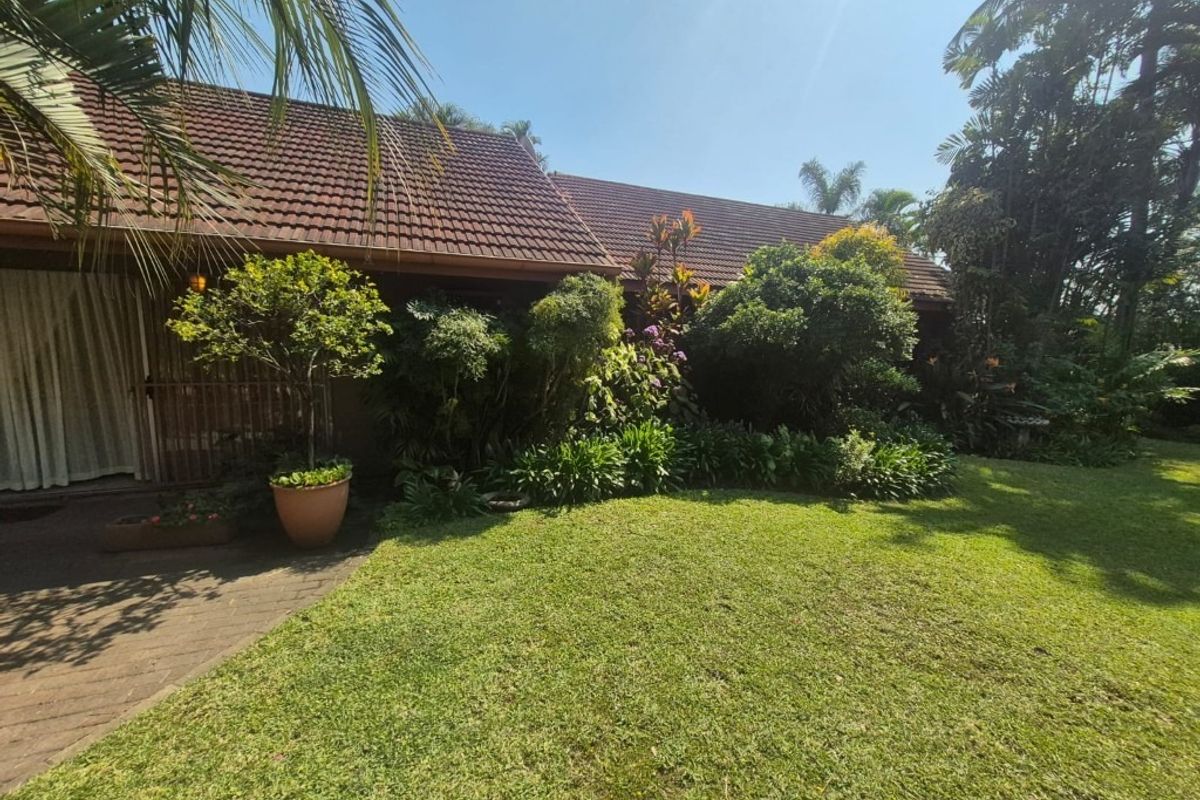 A view of the rear exterior of the house featuring a tiled roof, a paved patio area, and a well-maintained landscaped garden.