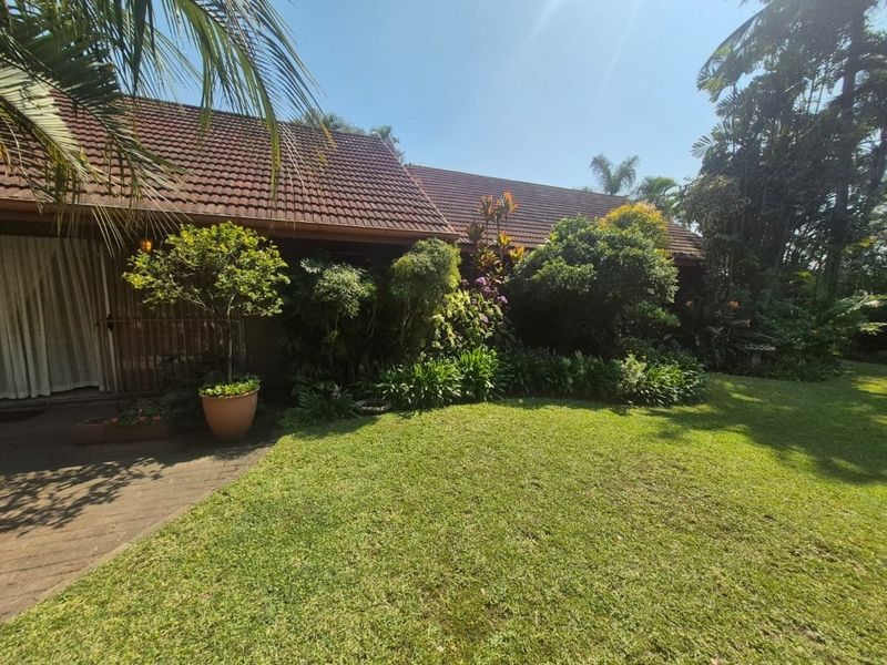 A view of the rear exterior of the house featuring a tiled roof, a paved patio area, and a well-maintained landscaped garden.
