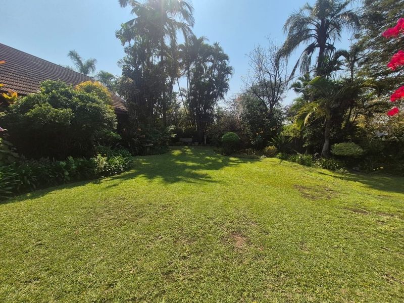 A spacious, well-maintained private garden featuring a large lawn area surrounded by mature trees and lush landscaping.