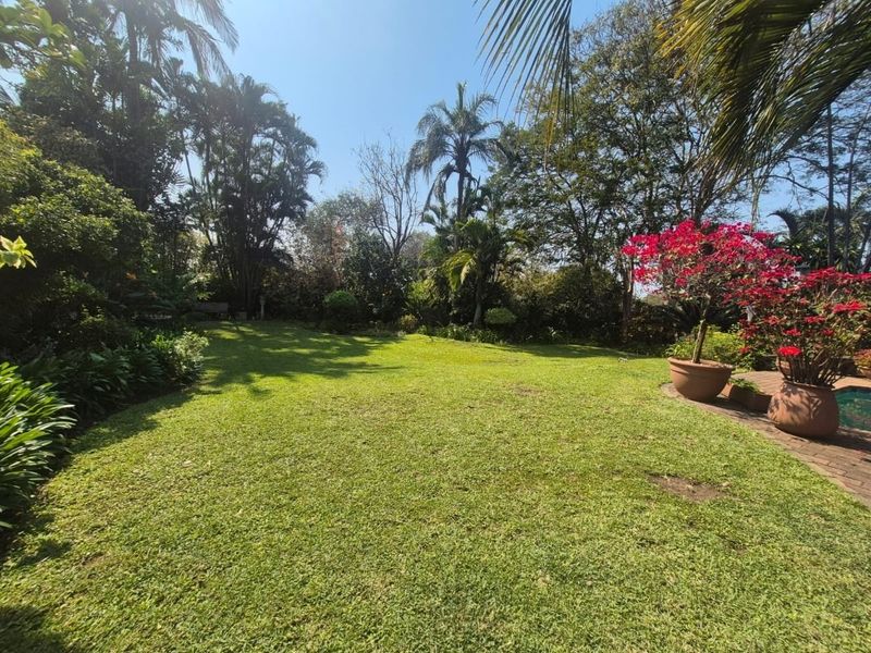 A spacious, well-maintained garden featuring a lush green lawn, mature trees, and established landscaping.
