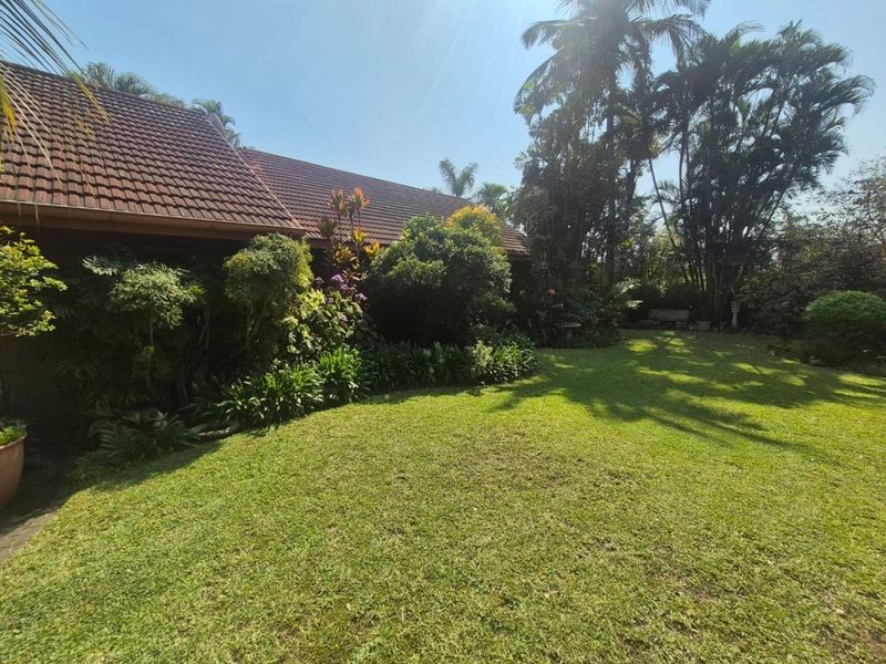 A well-maintained garden area featuring a lush lawn, mature trees, and a view of the property's tiled roofline.