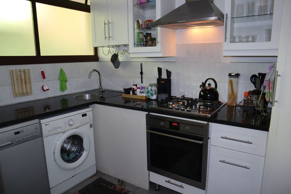 Compact kitchen featuring white cabinetry, black granite countertops, integrated gas hob, oven, extractor fan, and under-counter space for a washing machine and dishwasher.