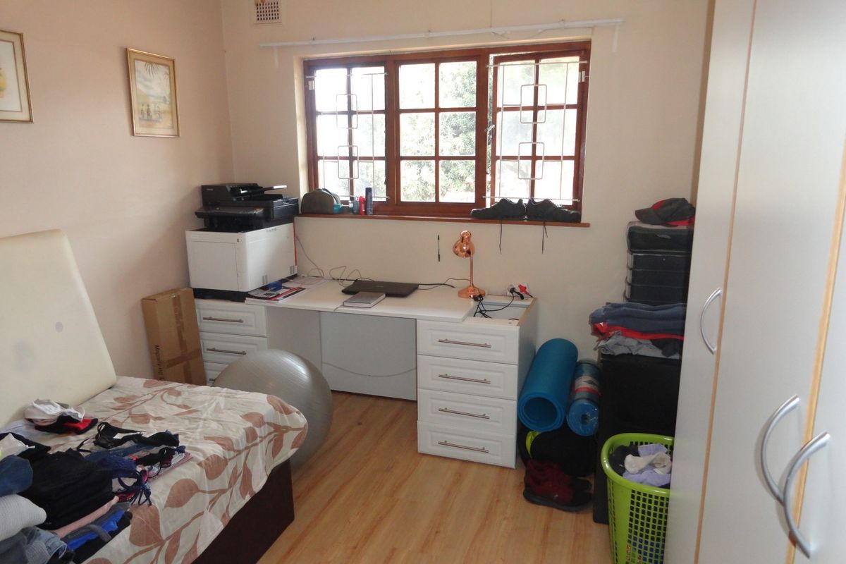A functional bedroom featuring laminate flooring, a built-in desk unit, and a window with security bars.