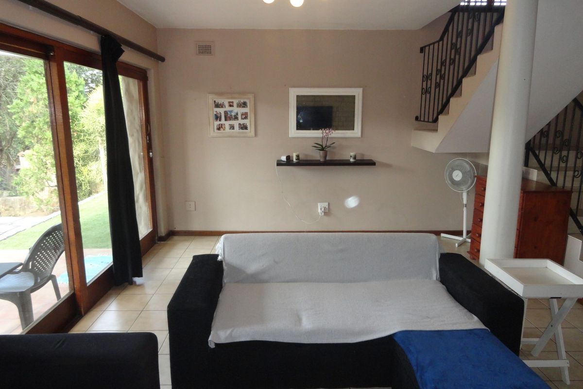 A living room featuring tiled flooring, a staircase with a metal railing, and large sliding glass doors providing access to the outdoor patio area.