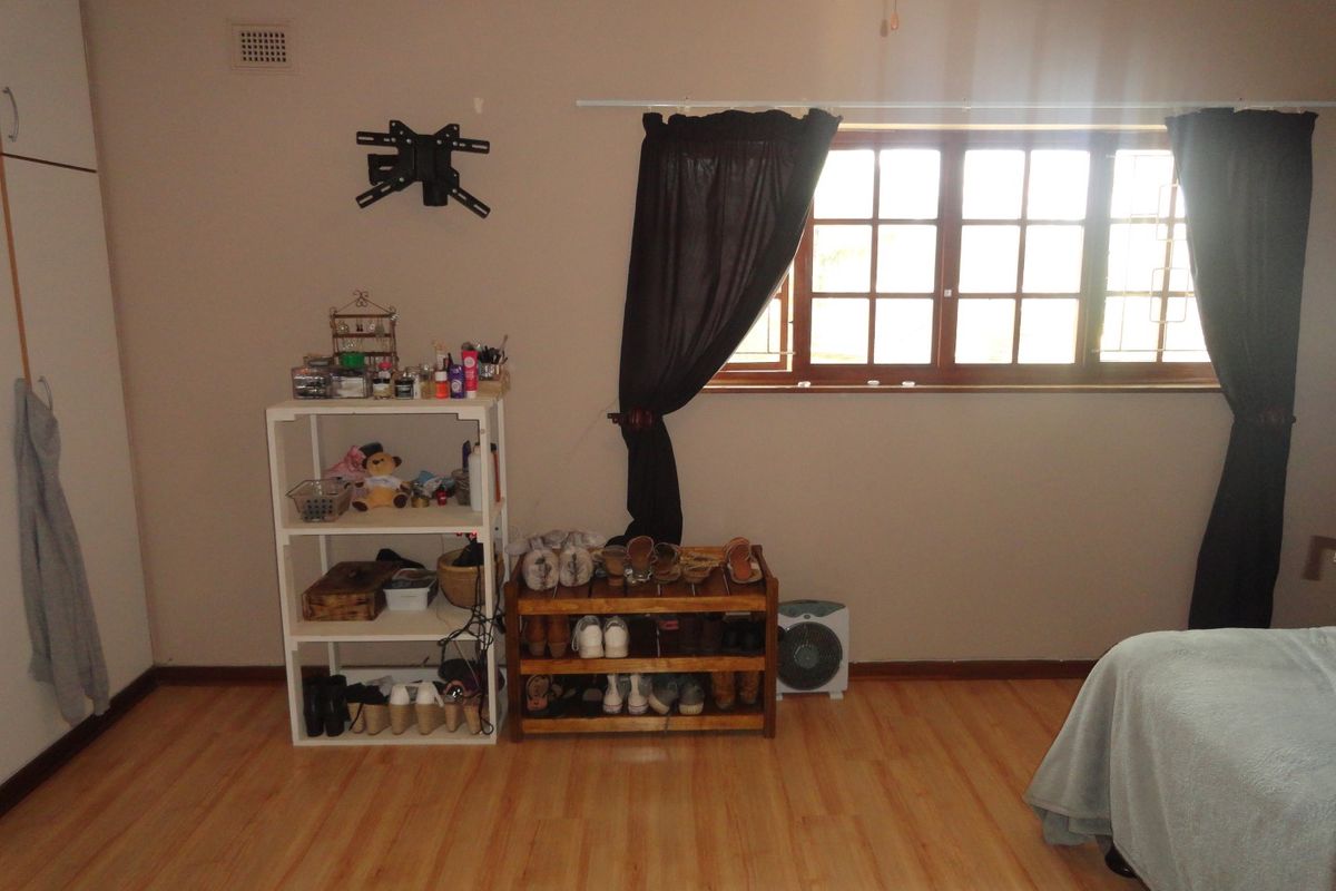 A bedroom featuring laminate flooring, built-in cupboards, and a window with wooden frames.