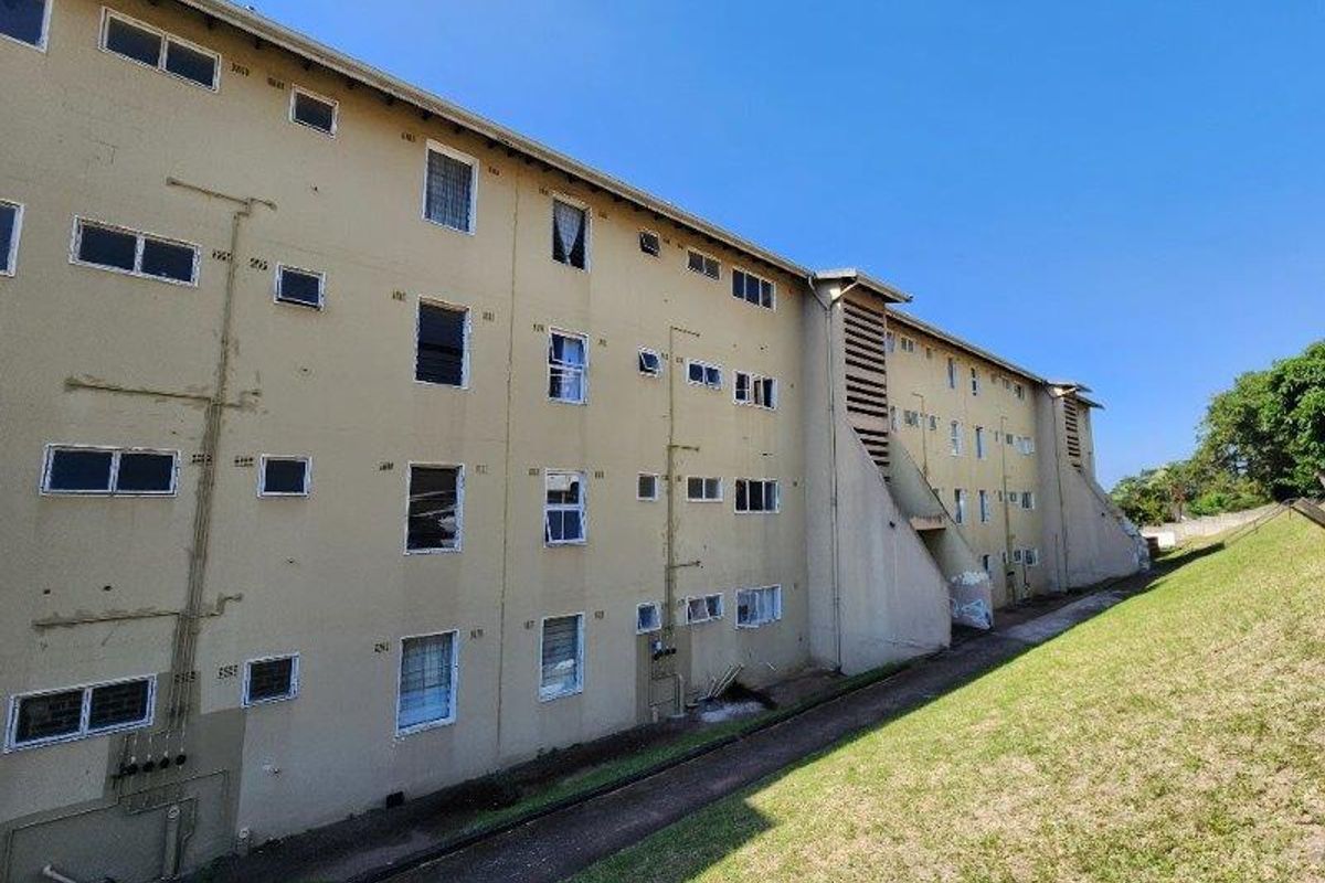 Exterior view of a multi-story apartment building facade showing multiple window units and external plumbing infrastructure.