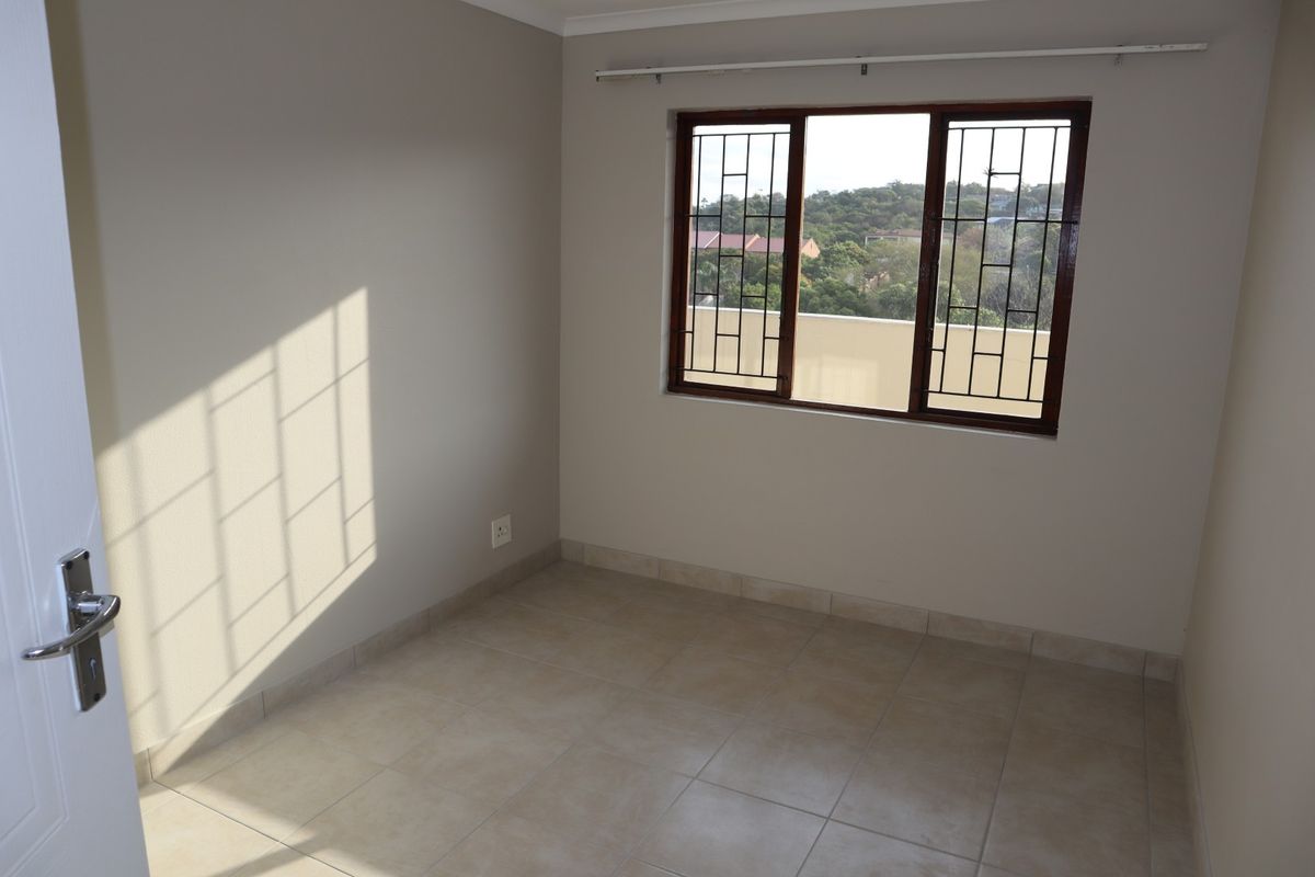 A bright, empty bedroom featuring neutral tiled flooring, security bars on the window, and a curtain rail, offering a clean canvas for personalization.
