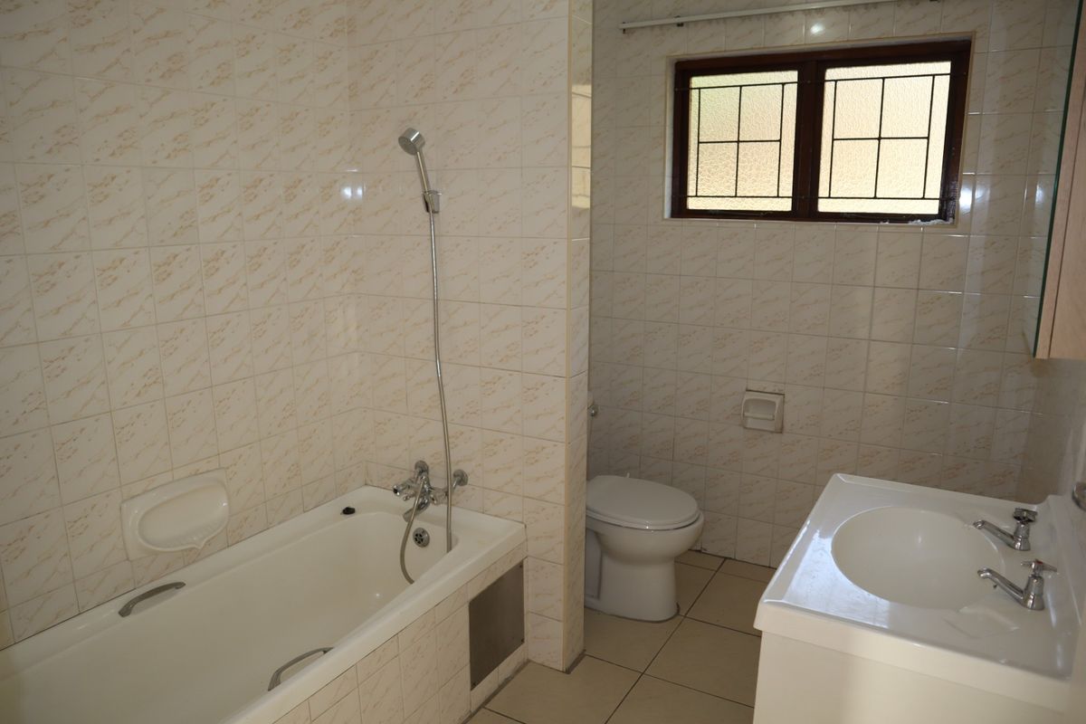 A functional bathroom featuring a bathtub with handheld shower, a toilet, and a vanity basin, finished with neutral wall and floor tiling.