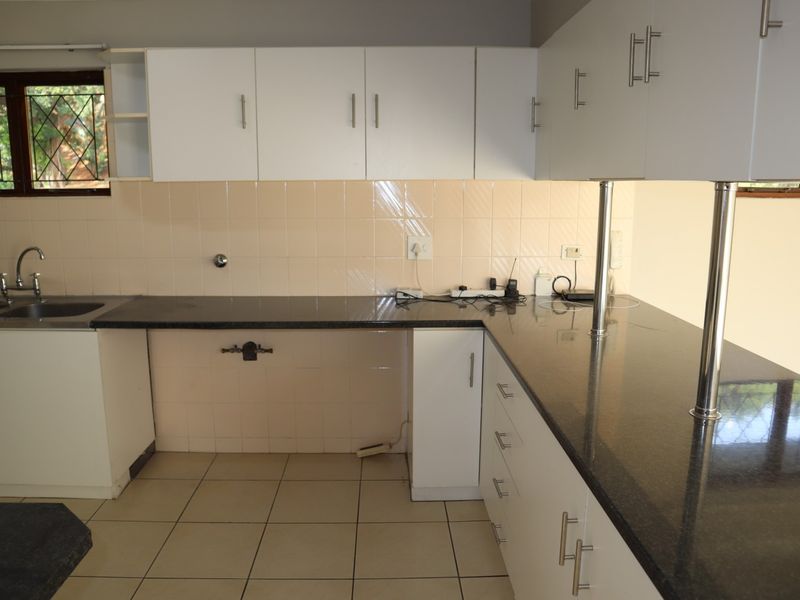 A functional kitchen featuring white cabinetry, dark granite countertops, tiled backsplash, and ceramic flooring, offering a clean and practical workspace.