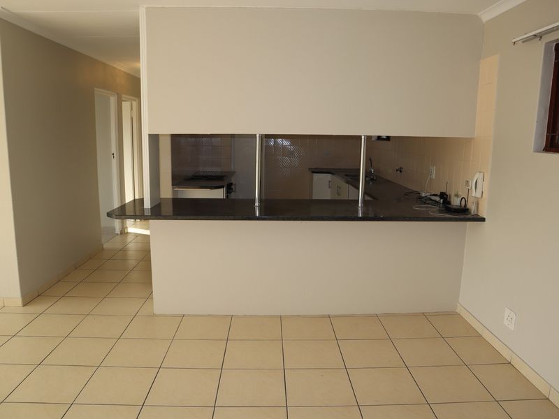 Open plan living area featuring a breakfast counter overlooking the kitchen with tiled flooring and neutral wall finishes.