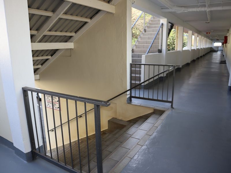 A functional apartment building hallway featuring a concrete staircase with metal railings and tiled flooring, providing access to multiple levels.