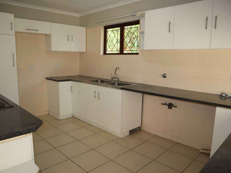 A functional kitchen featuring white built-in cabinetry, dark laminate countertops, tiled splashbacks, and a double bowl sink with a built-in hob.