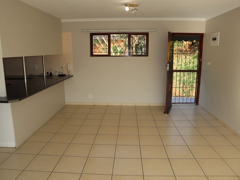 An open-plan living area featuring tiled flooring, a granite kitchen counter, and a secure entrance with a security gate.