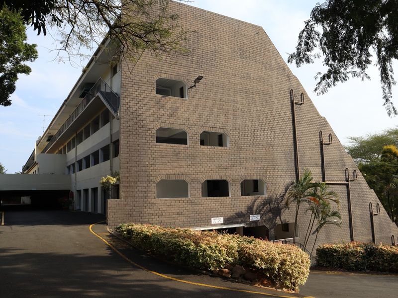 Exterior view of a multi-level apartment building featuring a brick facade, external staircases, and an asphalt driveway leading to the parking area.