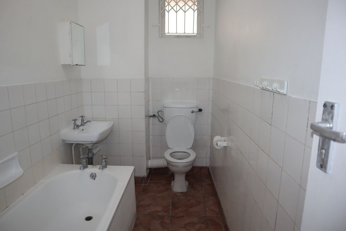A dated bathroom featuring a bathtub, pedestal basin, and toilet with white wall tiling and terracotta-style floor tiles.
