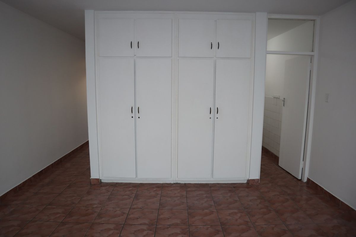 An empty bedroom featuring built-in white cupboards and tiled flooring, offering a clean and neutral space ready for personalization.