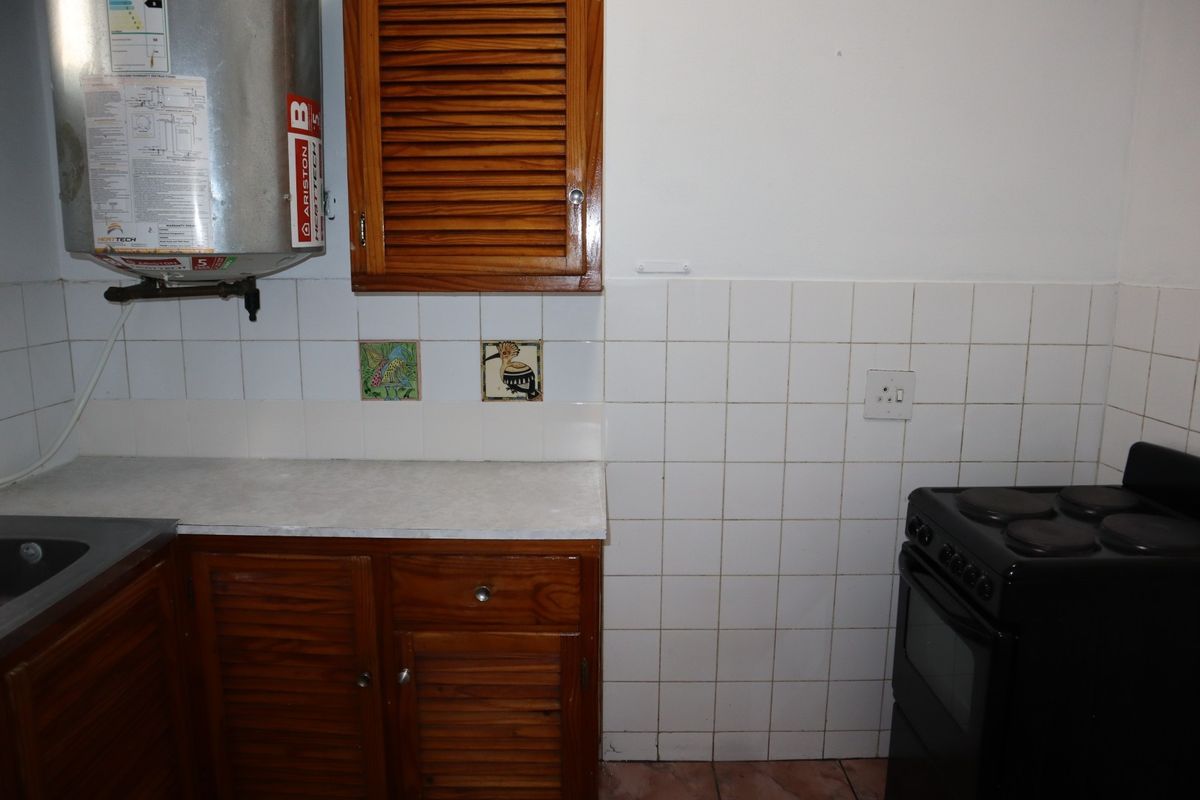A functional kitchen area featuring wooden cabinetry, a tiled backsplash, an electric stove, and a wall-mounted water heater.