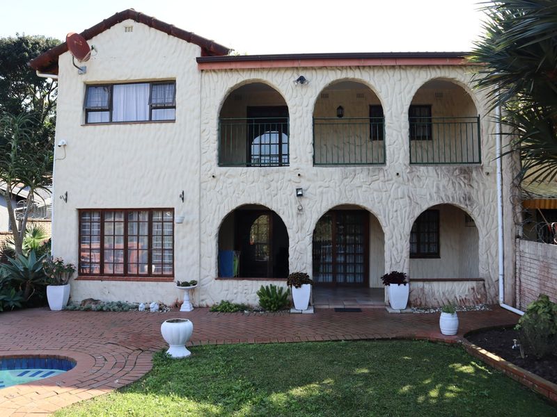 Rear elevation of a two-story townhouse featuring arched patios, a balcony with metal railings, brick paving, and a swimming pool.