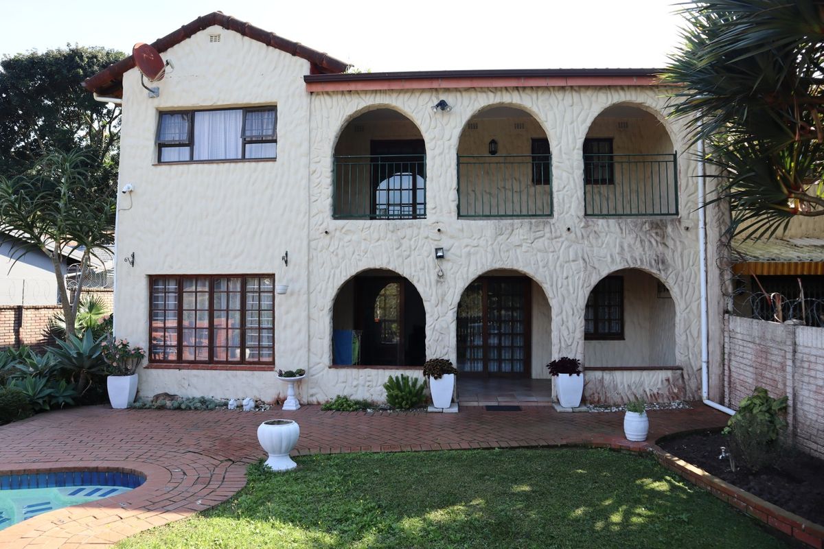 Rear elevation of a two-story townhouse featuring arched patios, a balcony with metal railings, brick paving, and a swimming pool.