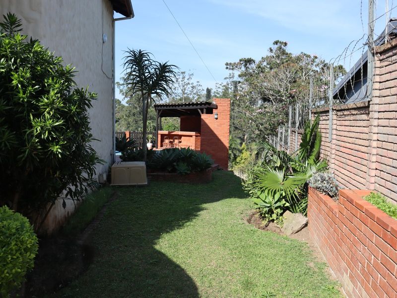 Rear garden area featuring a brick boundary wall with security fencing and a built-in brick braai area under a covered structure.