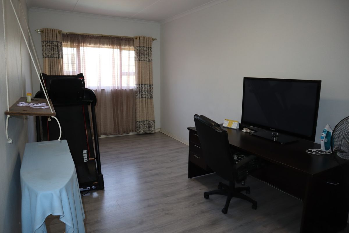 A functional bedroom space featuring light-toned laminate flooring and neutral wall finishes, suitable for use as a bedroom or home office.