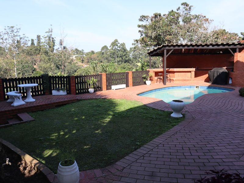 Outdoor entertainment area featuring a swimming pool, brick-paved patio, and a covered built-in brick bar, set within a landscaped garden with scenic views.