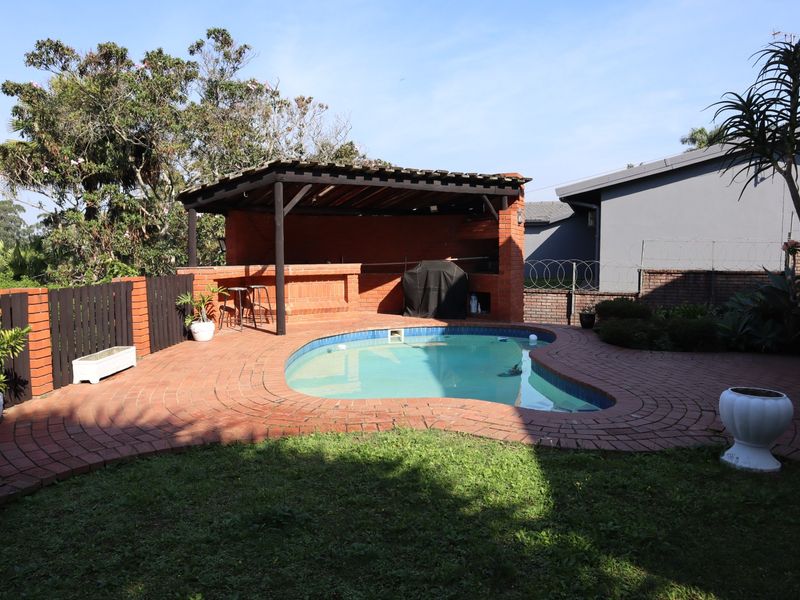 Outdoor pool area featuring a kidney-shaped swimming pool, brick paved surround, and a covered brick built-in braai area under a timber pergola.