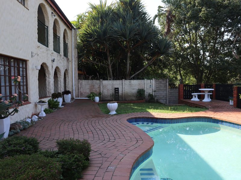Rear exterior view of the townhouse featuring a swimming pool, brick paved patio area, and a multi-level facade with arched balcony details.