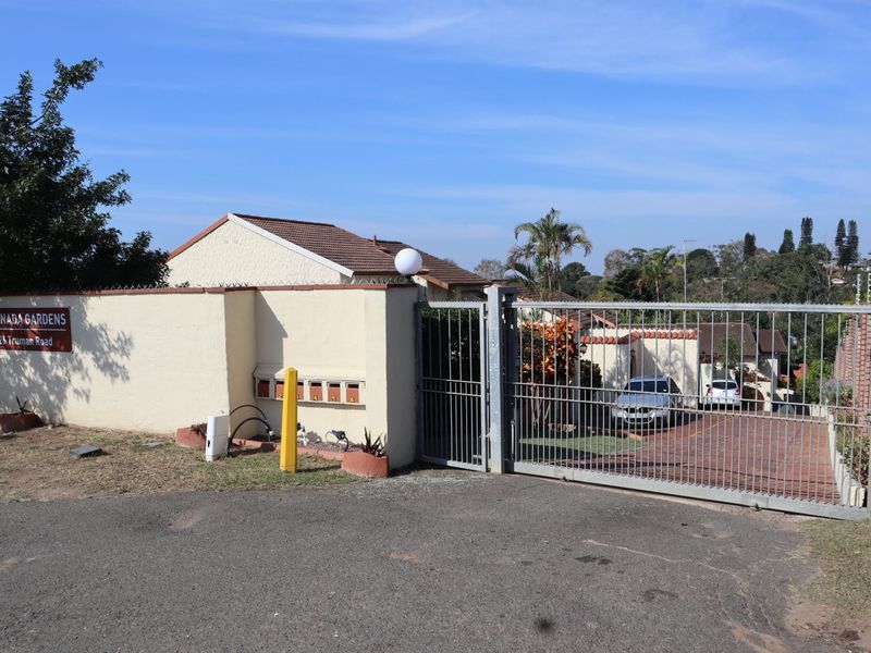 Front entrance view of Granada Gardens townhouse complex featuring a secure gated access point, perimeter wall with electric fencing, and paved driveway.