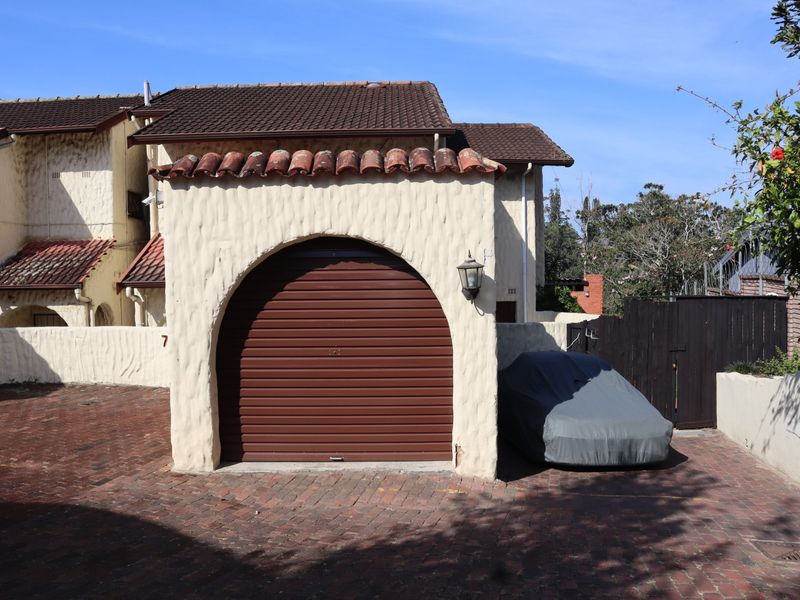 A townhouse garage featuring a distinctive arched roller shutter door, tiled roof, and brick paved driveway in a residential setting.