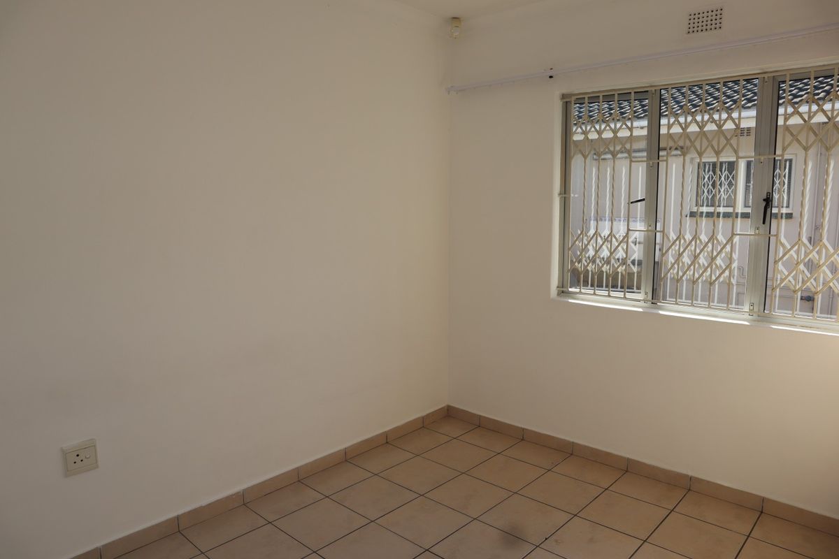 An empty bedroom featuring tiled flooring, a window with security bars, and a fitted security gate.